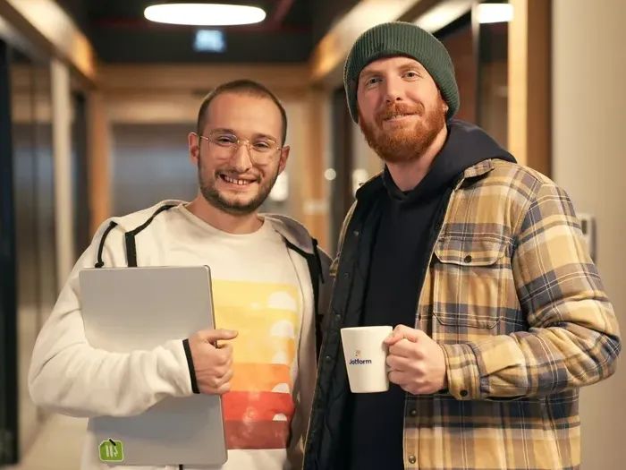 Two smiling colleagues in a modern office hallway, holding a laptop and mug, reflecting community on Local Directory Central